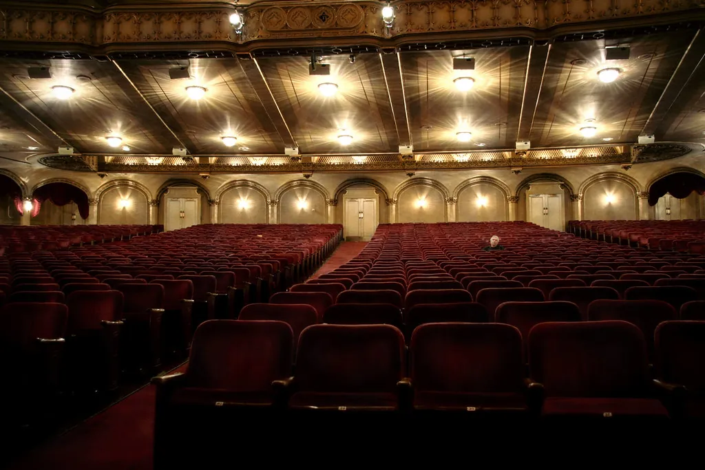 Teatro casi vacío con filas de butacas rojas bajo lámparas encendidas